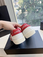 Close-up of low-top sneakers: white uppers with red heel tabs and tan soles