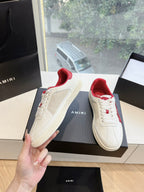 White low-top sneakers with red lining and red logo detail, held by a hand