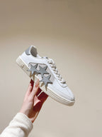 White sneaker with oversized star print and textured outsole, lace-up, held up.