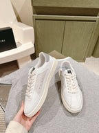 White low-top sneakers with side stripes and black logo, lace-up, held in hand.