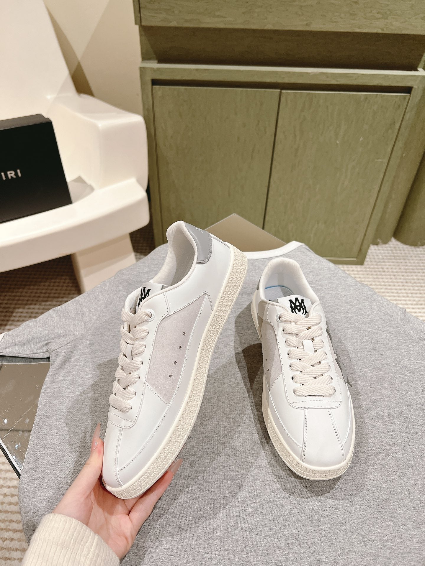 White low-top sneakers with side stripes and black logo, lace-up, held in hand.