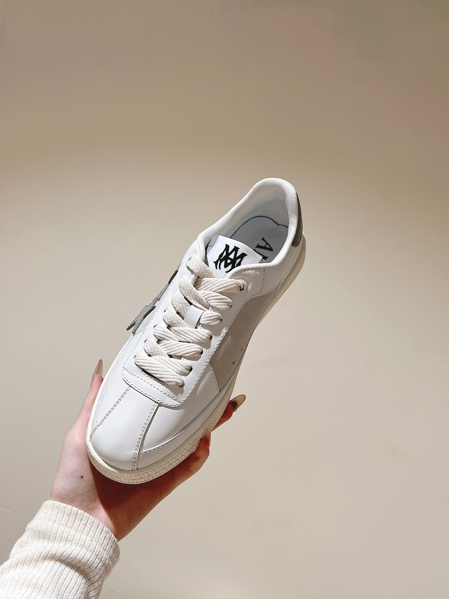 White low-top sneaker with black logo on tongue, side profile, lace-up, held up.