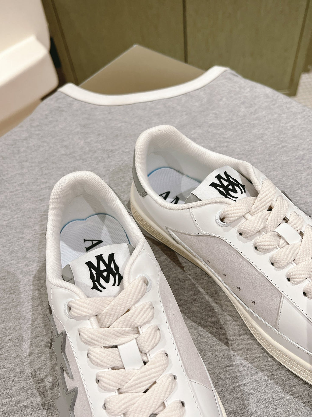 White low-top sneakers with black logo on tongue and side, lace-up, close view.