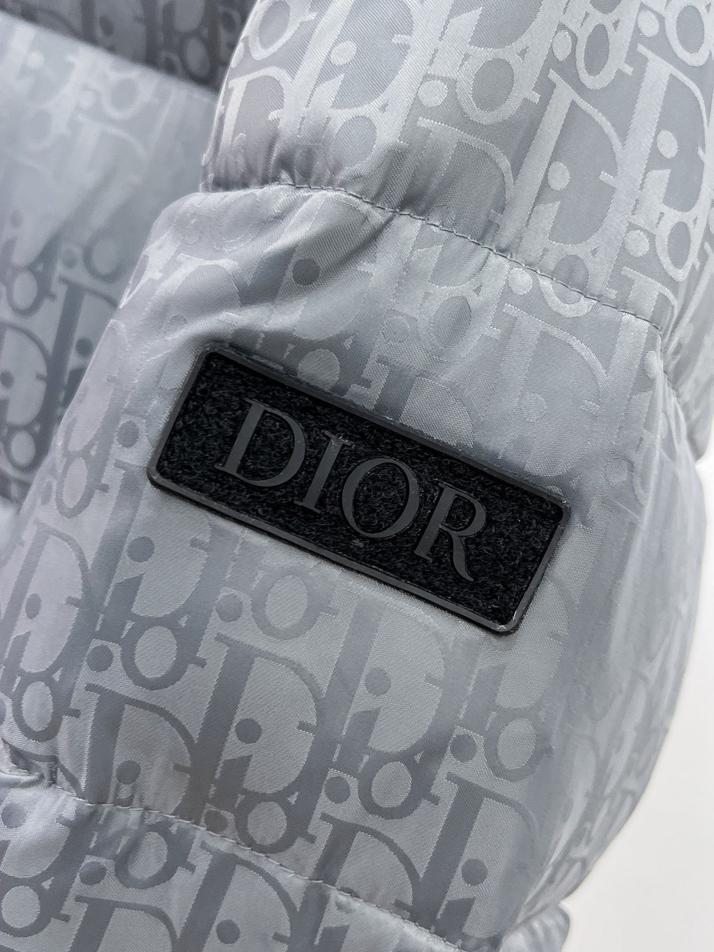 Long puffer jacket detail of black Dior logo patch on gray-blue monogram