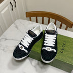 Pair of black and white Gucci low-top sneakers with white laces and metallic accents