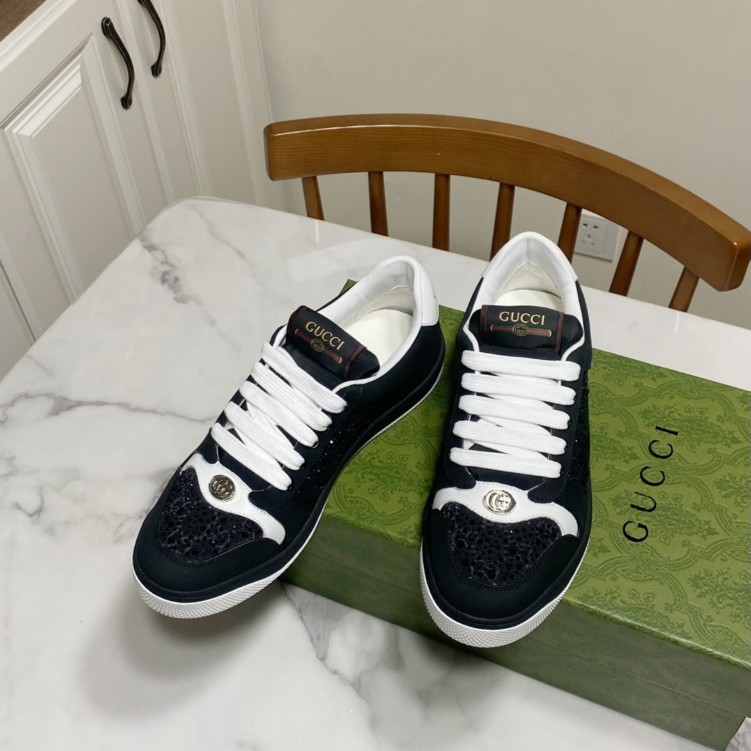 Pair of black and white Gucci low-top sneakers with white laces and metallic accents