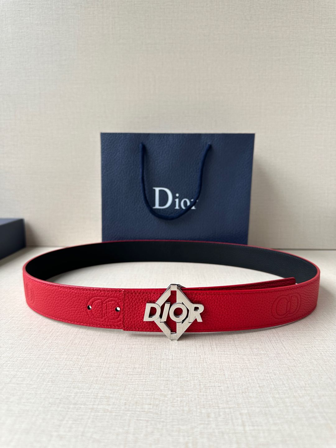 Red Dior belt with silver buckle and embossed logo on textured leather strap.