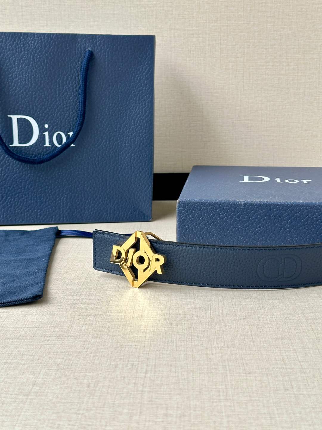 Dark blue leather belt with gold Dior logo buckle near Dior gift bags.