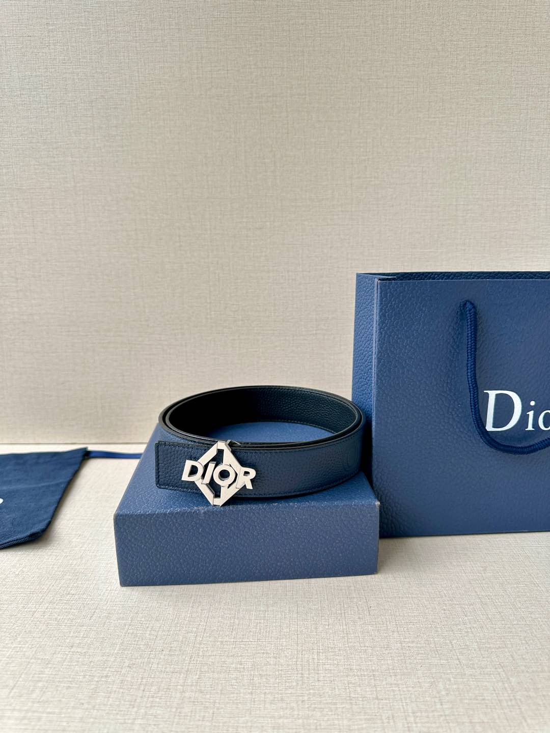 Dark blue leather belt with Dior logo buckle resting on blue gift boxes.