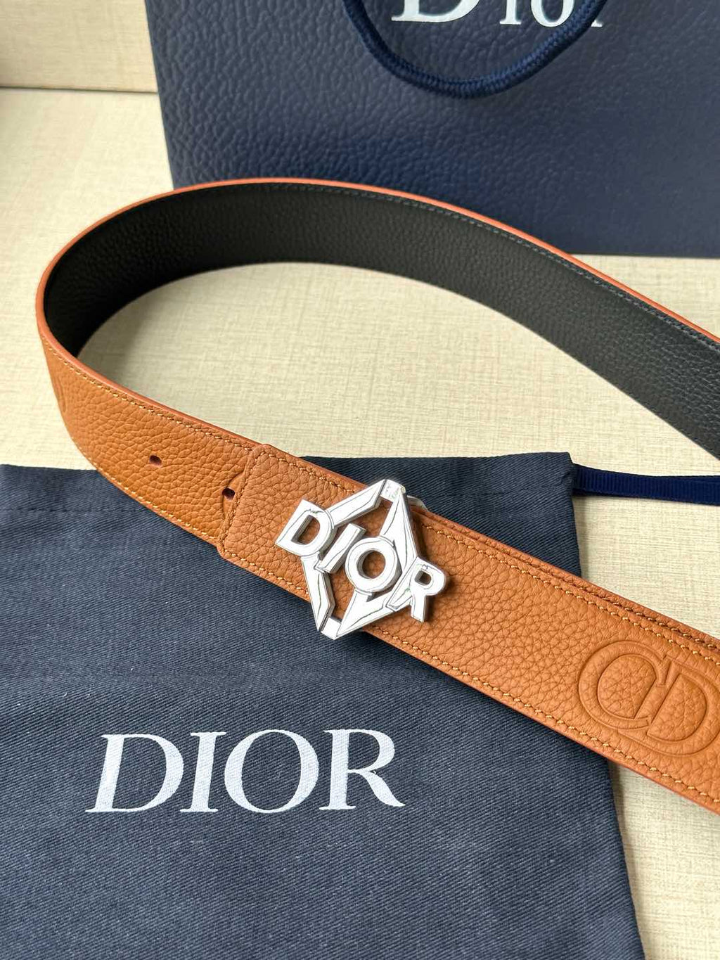 Dior belt close-up: tan strap with silver logo buckle and embossed pattern
