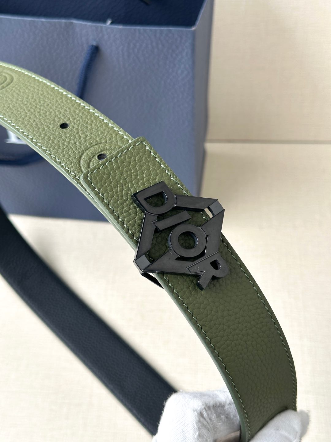 Dior leather belt close-up: olive strap with dark buckle and metal logo detail