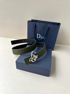 Dior leather belt shown with olive strap and dark logo buckle on a bag stand