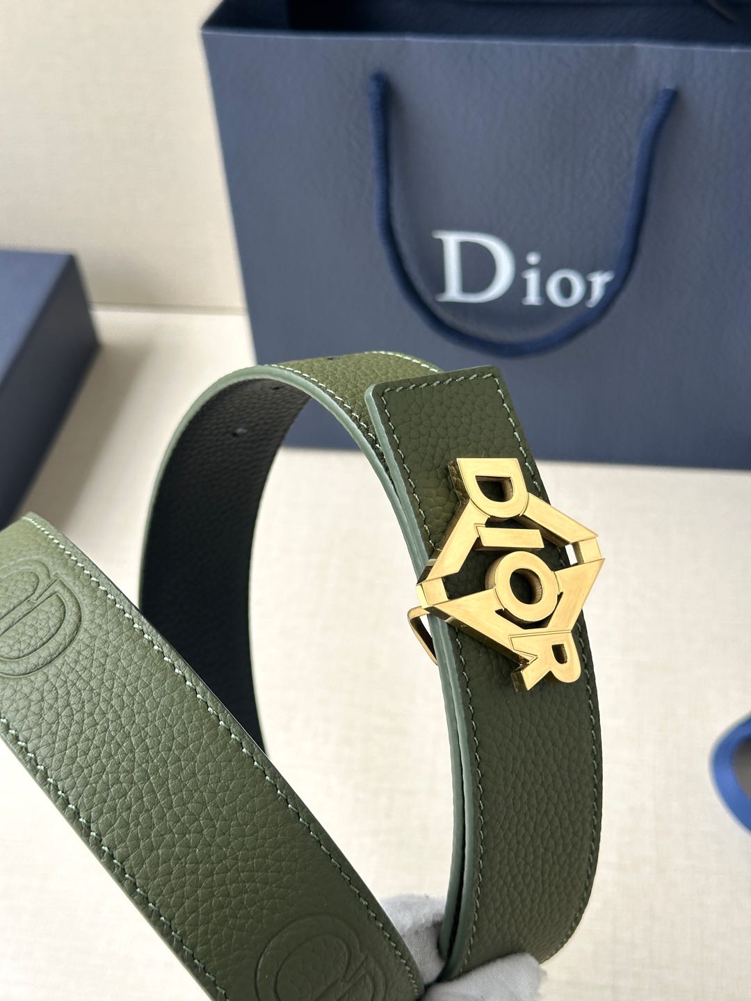 Dior leather belt close-up: olive strap and gold Dior buckle with raised lettering