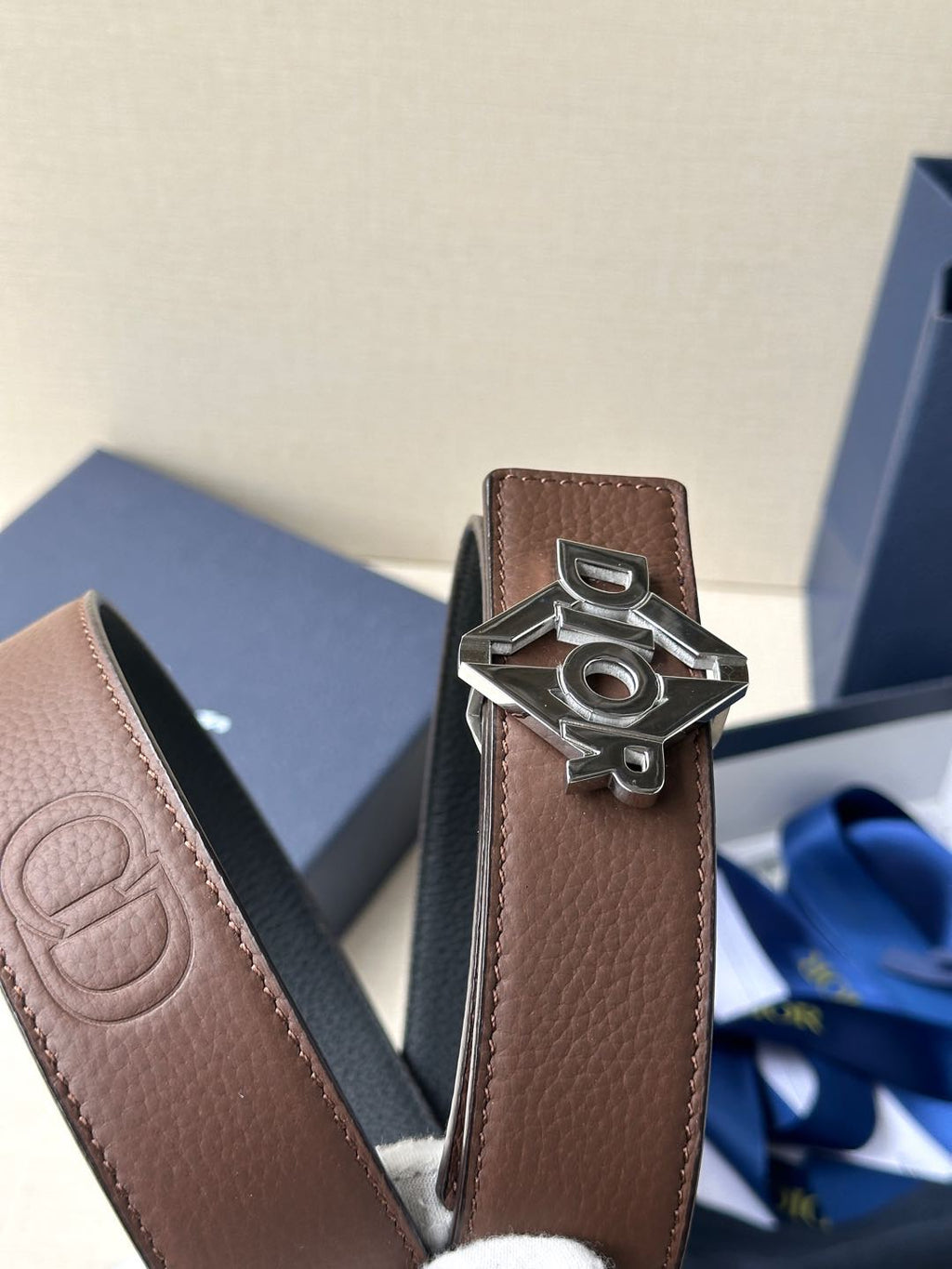 Dior belt close-up: brown leather strap with metallic Dior logo buckle.
