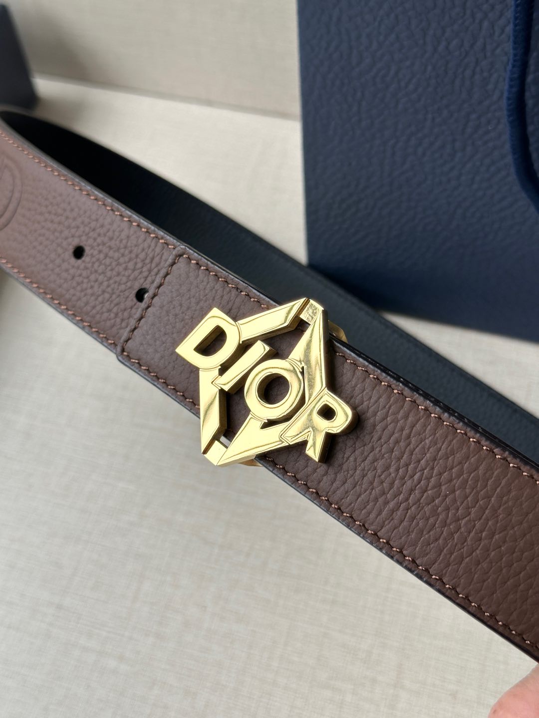 Dior belt detail: dark brown leather strap with gold-tone Dior logo buckle.