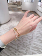 Pearl and gold charm bracelet on wrist with oval link and small pendant