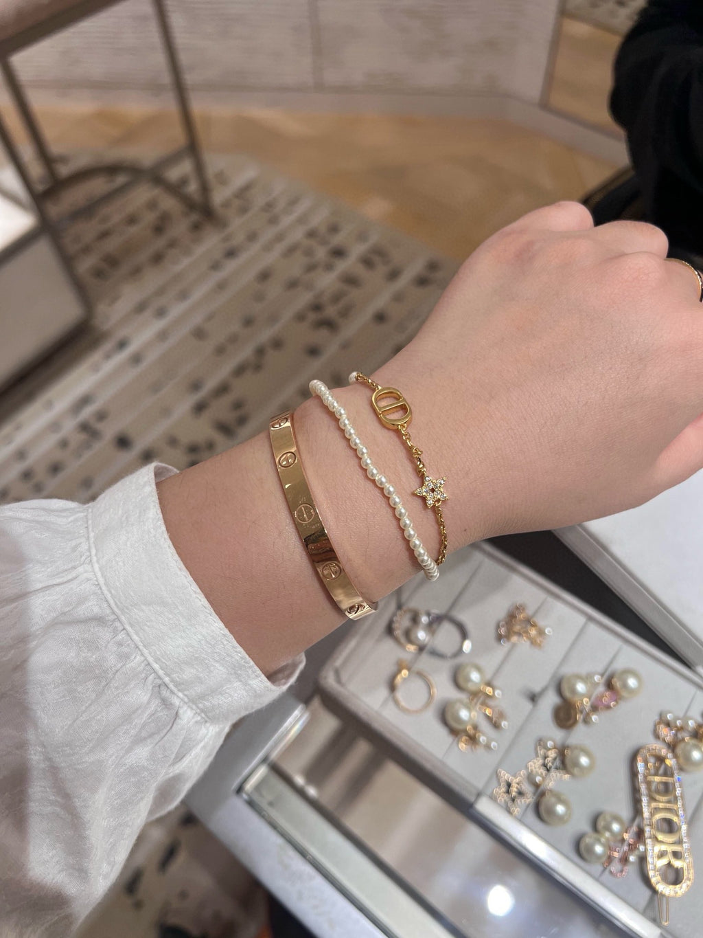 Pearl and gold charm bracelet on wrist with oval DIOR link and star charm