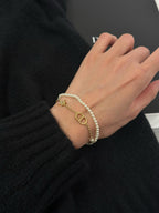 Pearl and gold charm bracelet on wrist with D-style pendant and star accents