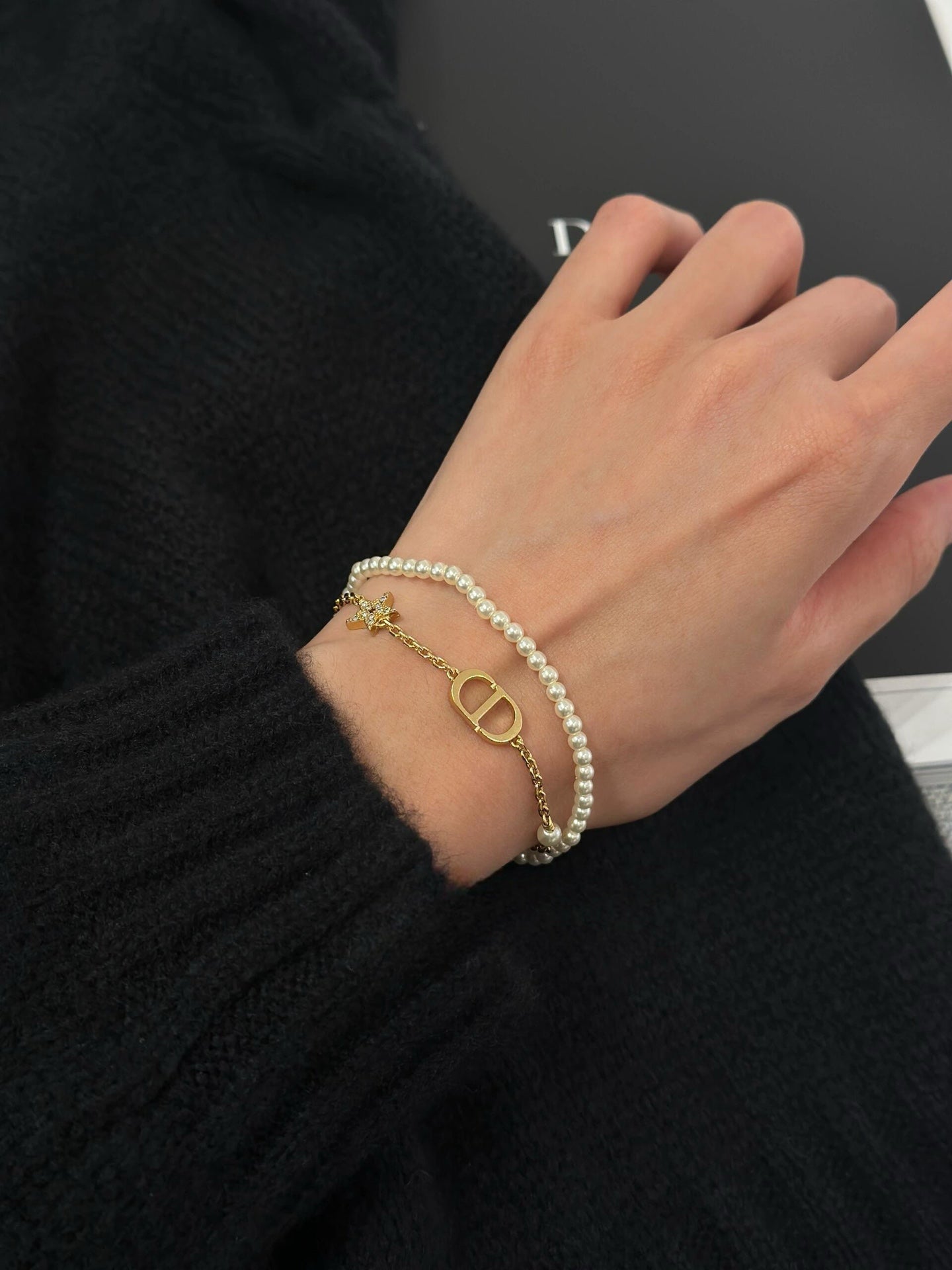 Pearl and gold charm bracelet on wrist with D-style pendant and star accents