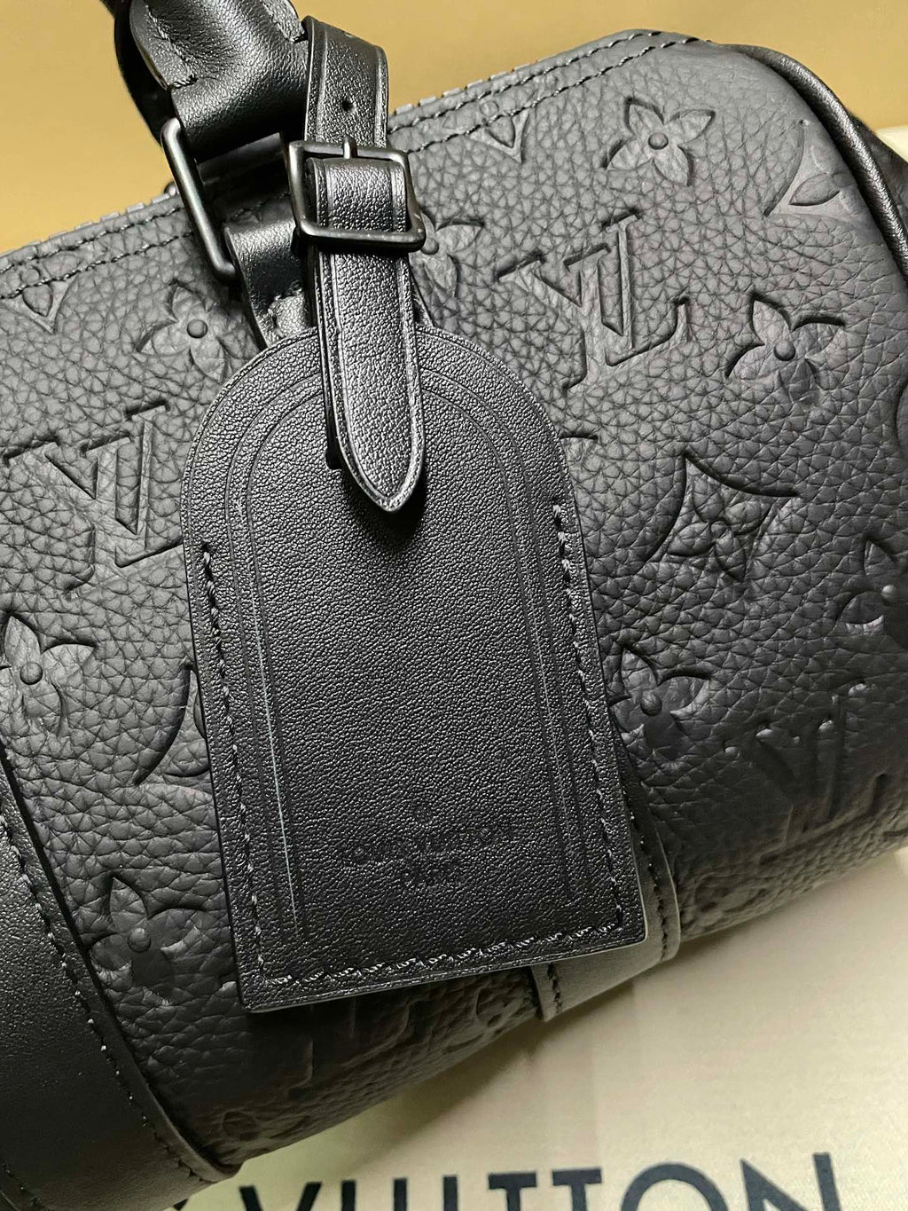 Monogram leather bag detail: zip pull and stitched leather tag on dark leather