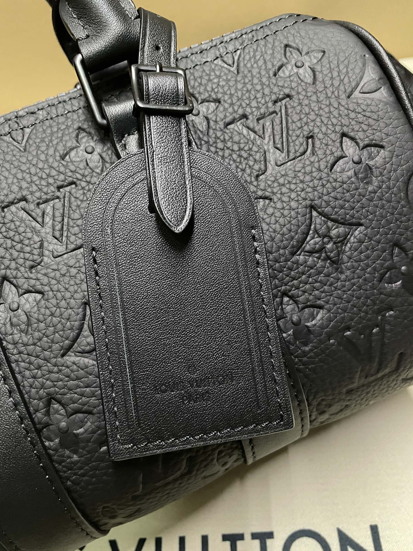 Monogram leather bag detail: zip pull and stitched leather tag on dark leather