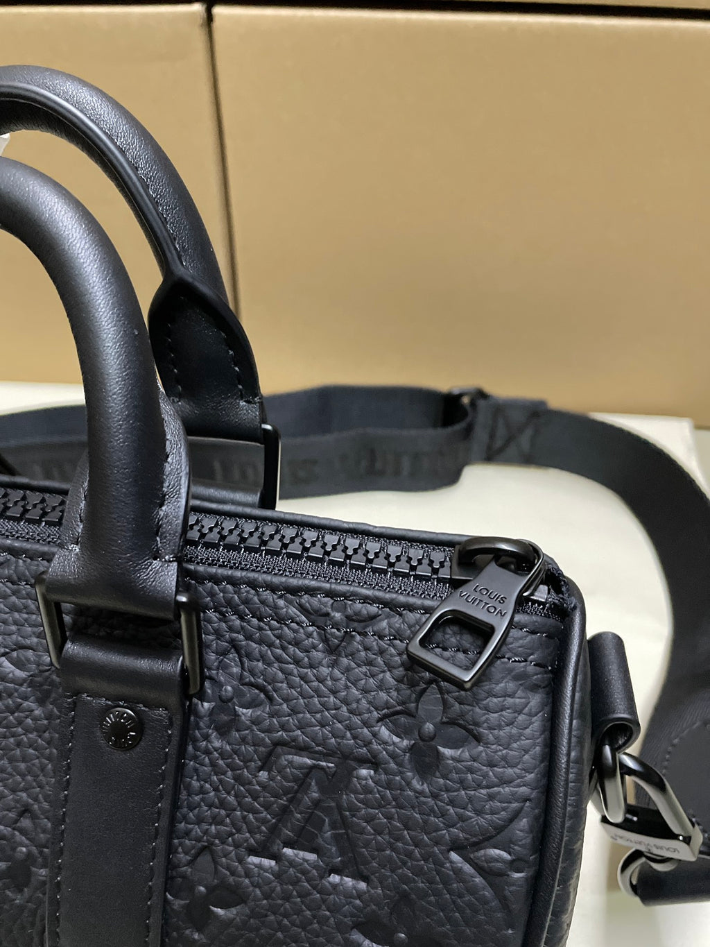 Monogram leather bag close-up: top handle, tab hardware, and metal buckle, dark leather