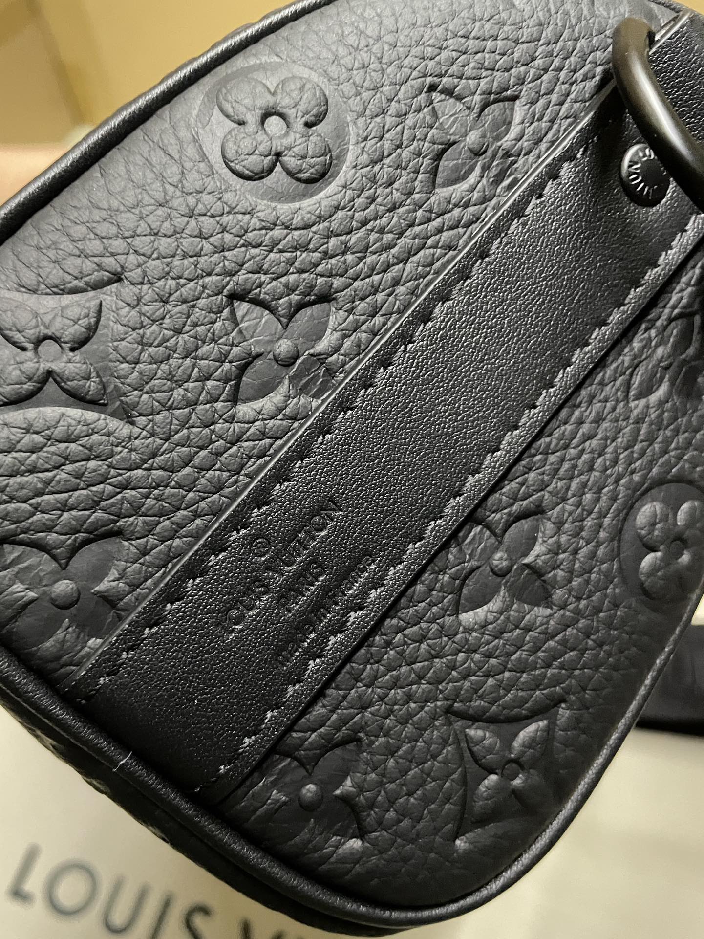 Monogram leather pouch detail with embossed flower pattern and stitched trim, dark leather
