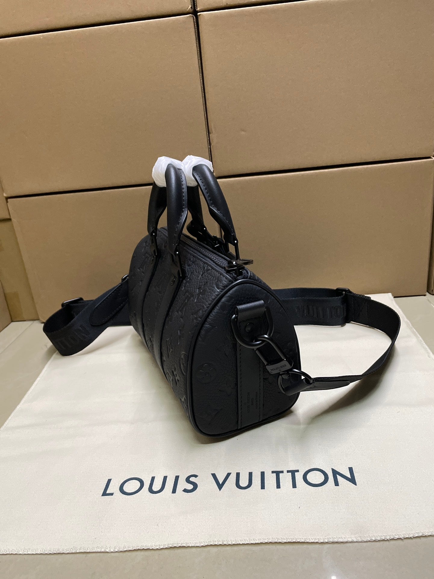 Monogram duffel bag side view with shoulder strap, metal rings, dark leather