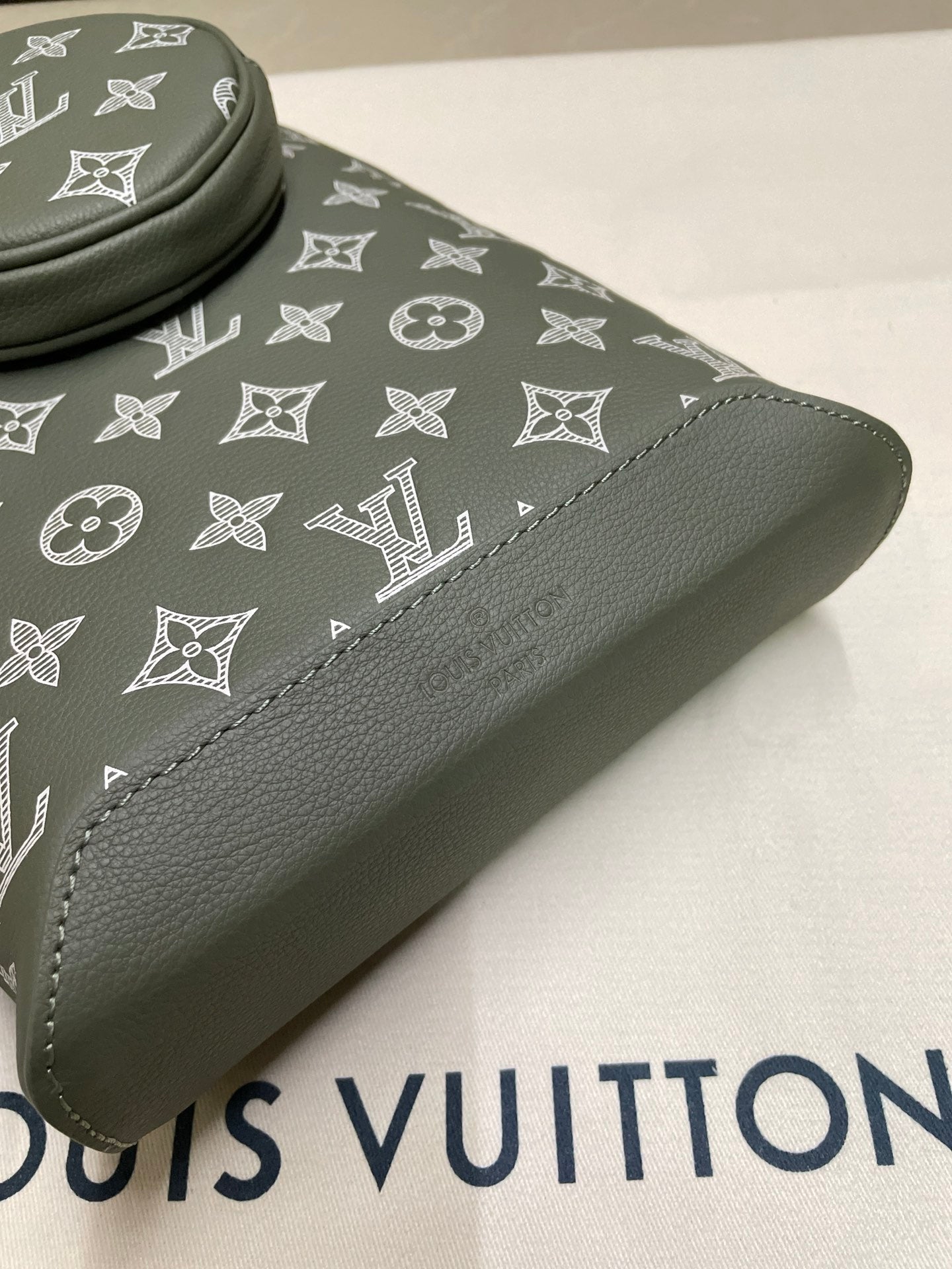 Louis Vuitton sling bag close-up, dark olive patterned canvas with stitched leather trim