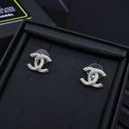 Pair of silver-tone Chanel CC stud earrings with rhinestone trim on dark display
