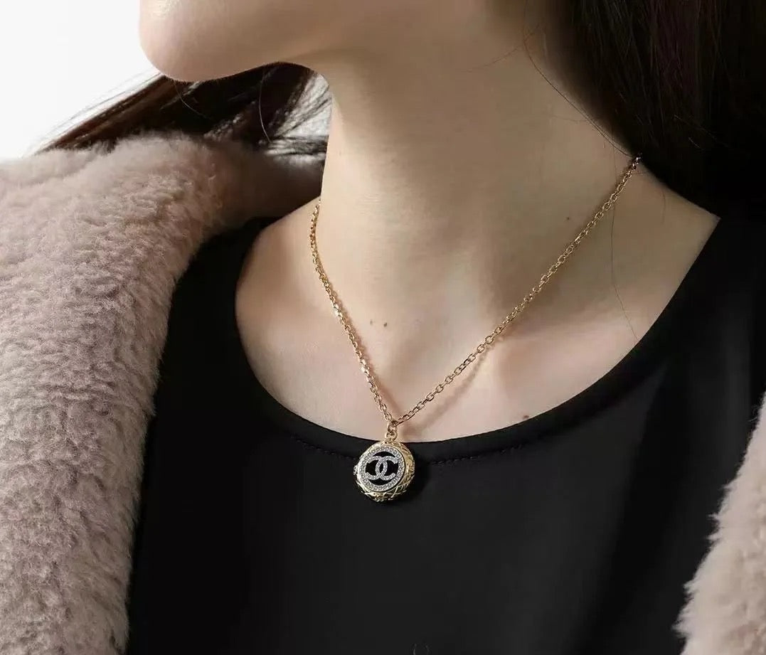 Gold-tone Chanel CC pendant necklace worn with black top and faux-fur jacket