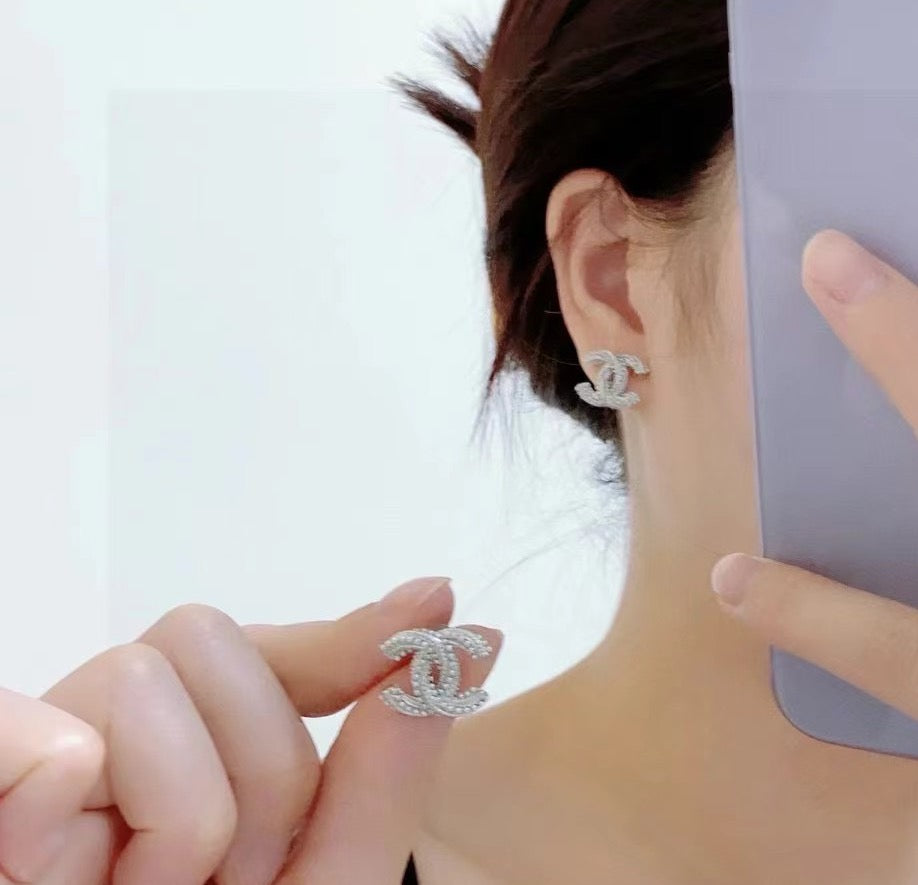 Chanel CC charm ring held near ear wearing a silver-tone stud earring