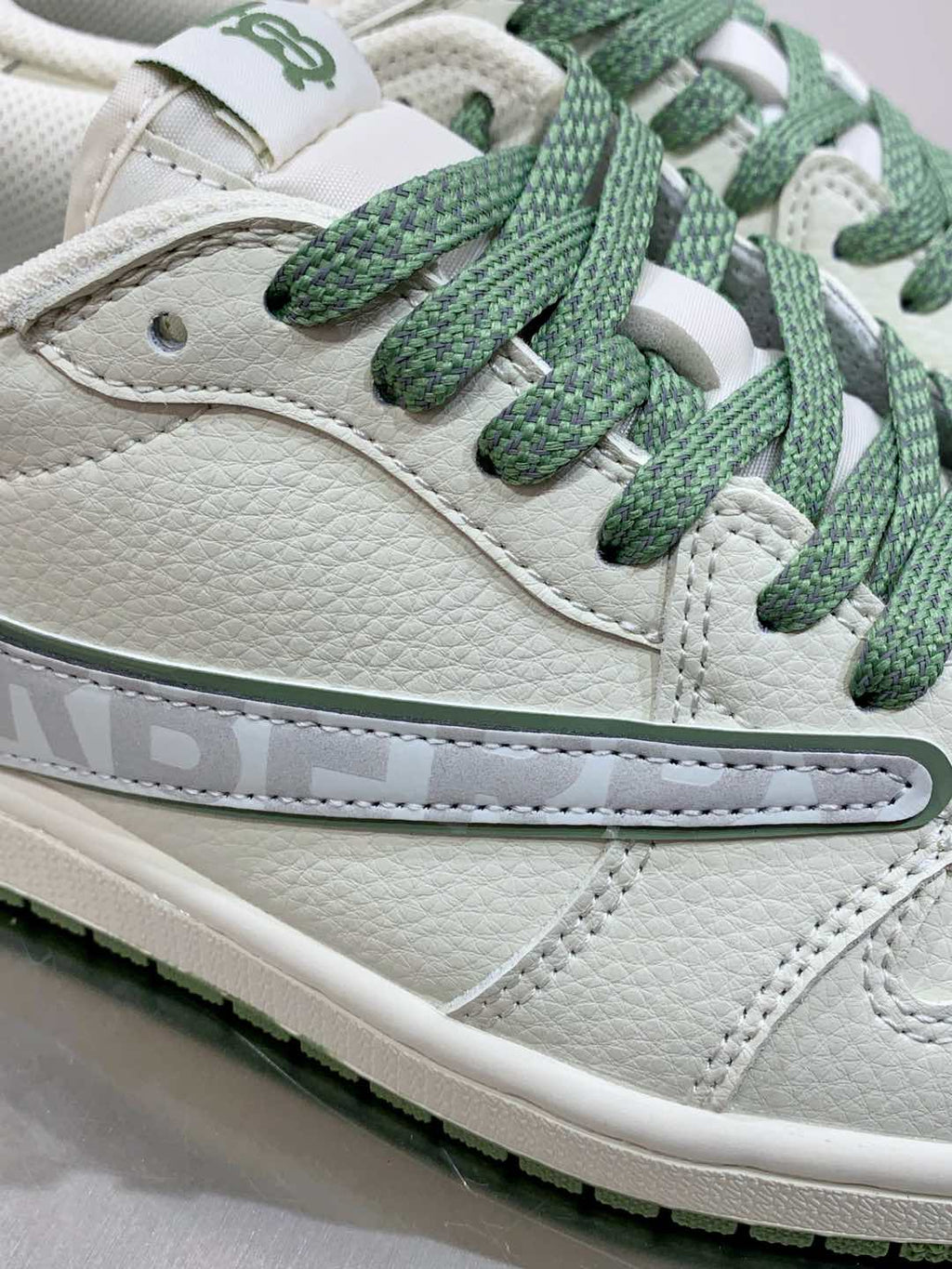 Burberry sneaker side close-up, white leather with green laces and stitched swoosh