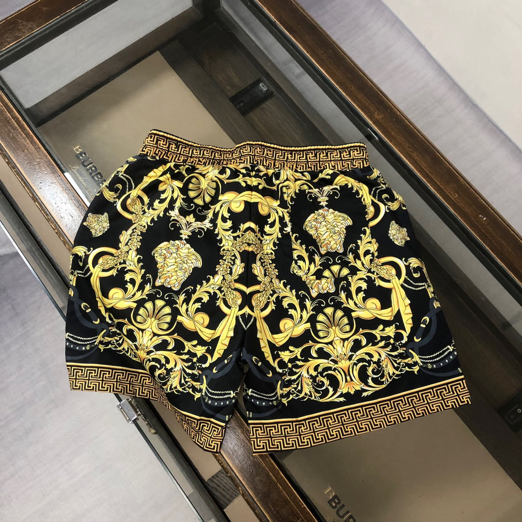 Black and gold baroque patterned shorts with Greek key border, laid flat in a box.