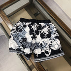 Printed shorts with black base, white baroque figures, drawstring waist, and trim hem