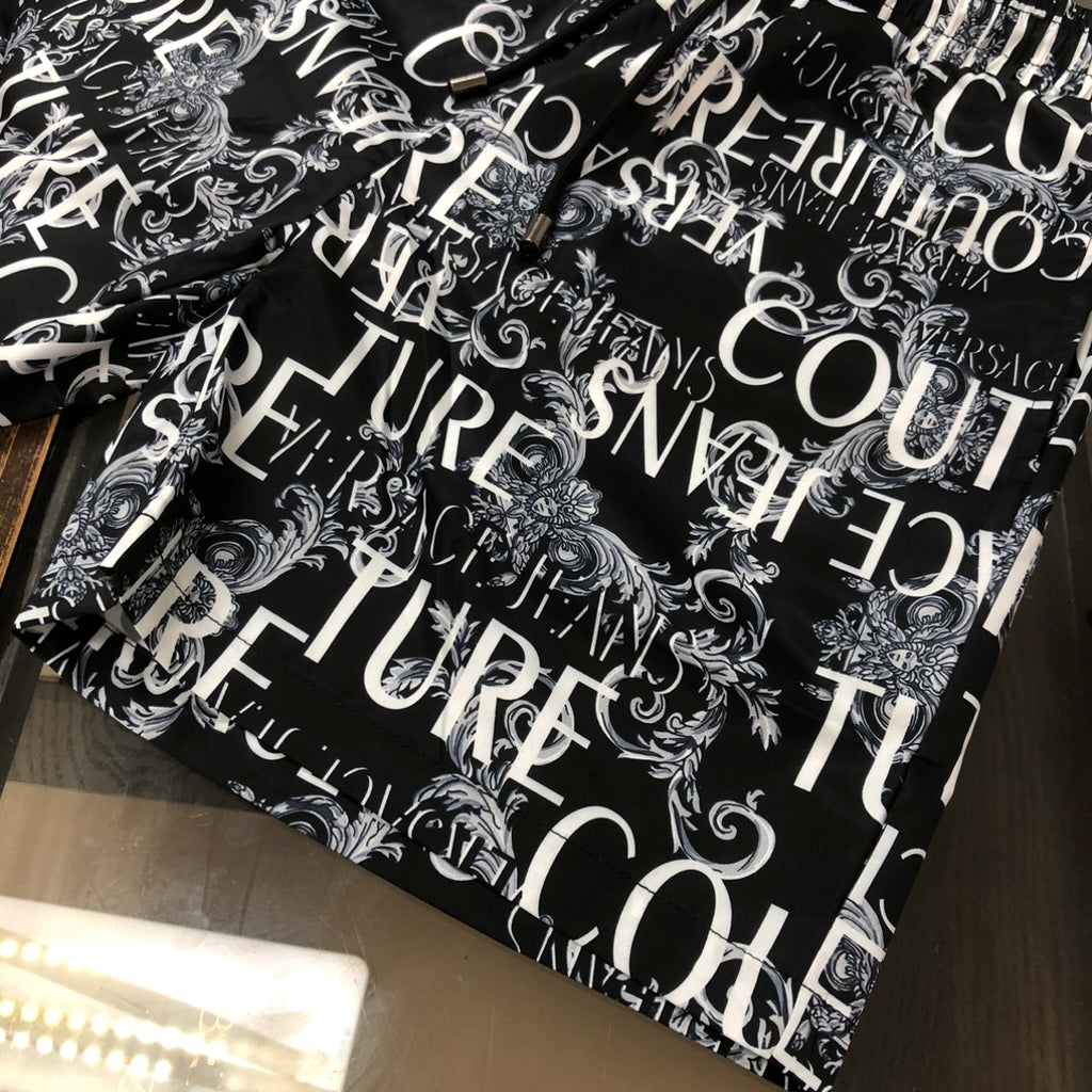 Versace shorts laid flat in black with white ornamental logo pattern allover.