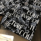 Versace shorts laid flat in black with white ornamental logo pattern allover.