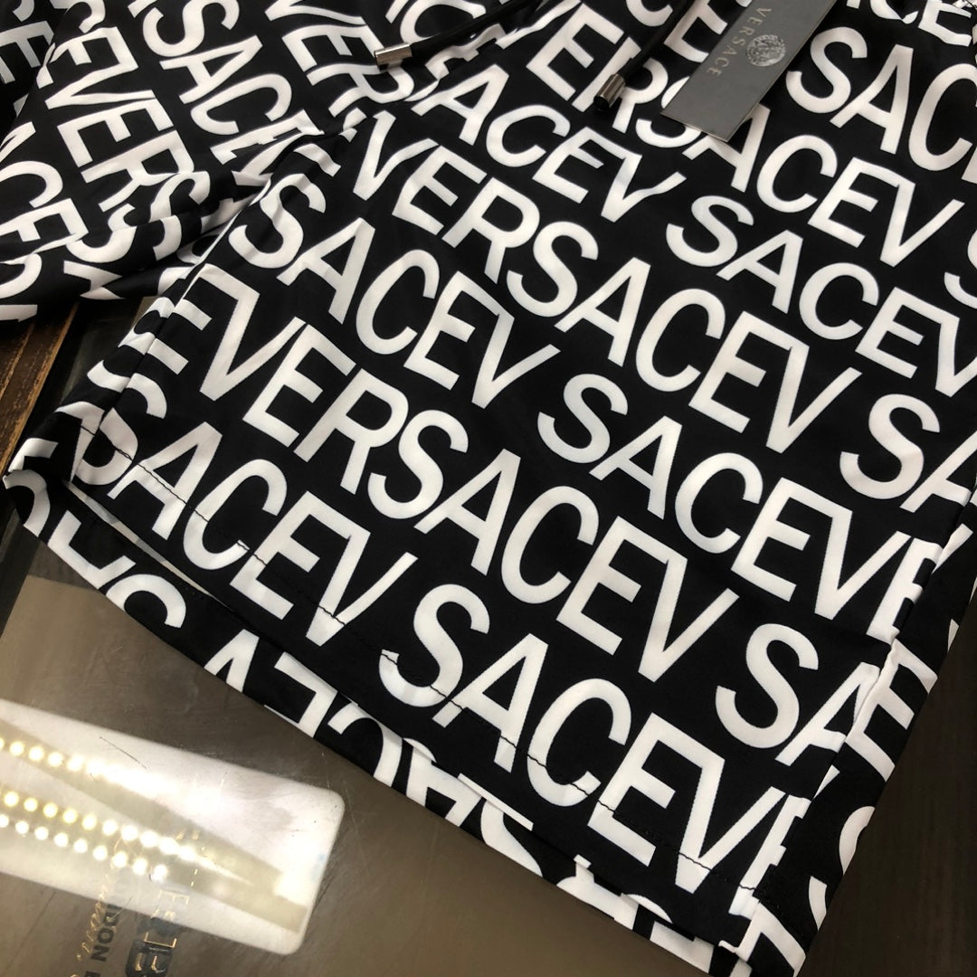 Versace logo shorts laid flat in black with white repeating VERSACE print
