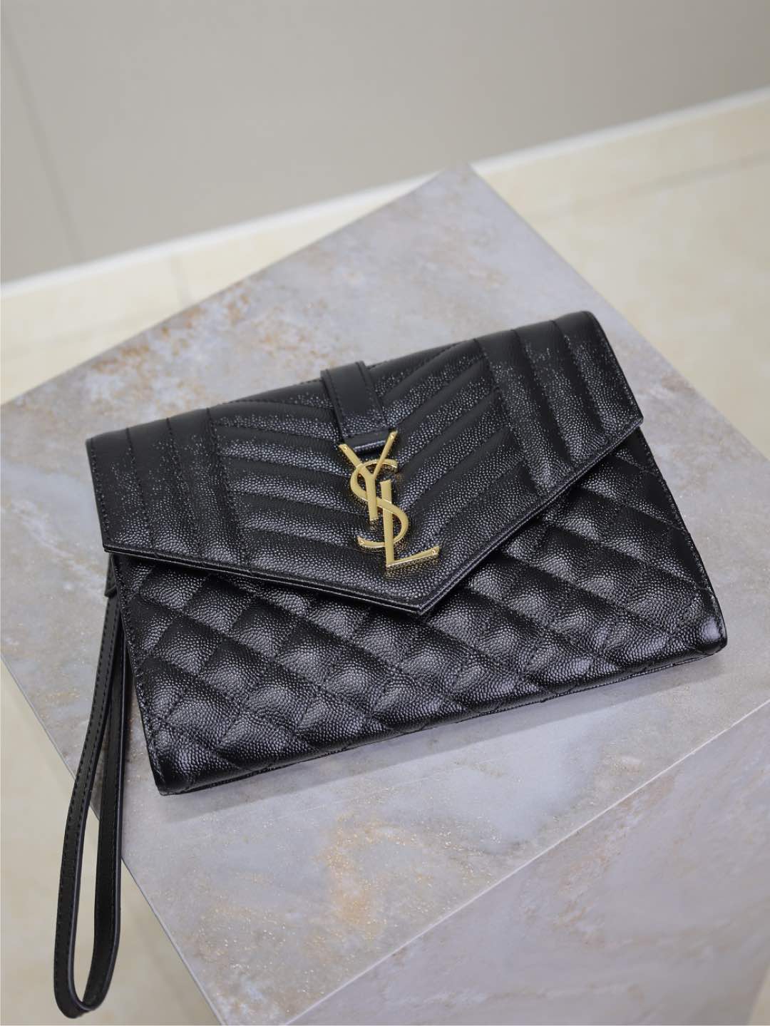 YSL small black quilted leather clutch-style bag with flap and gold YSL logo.