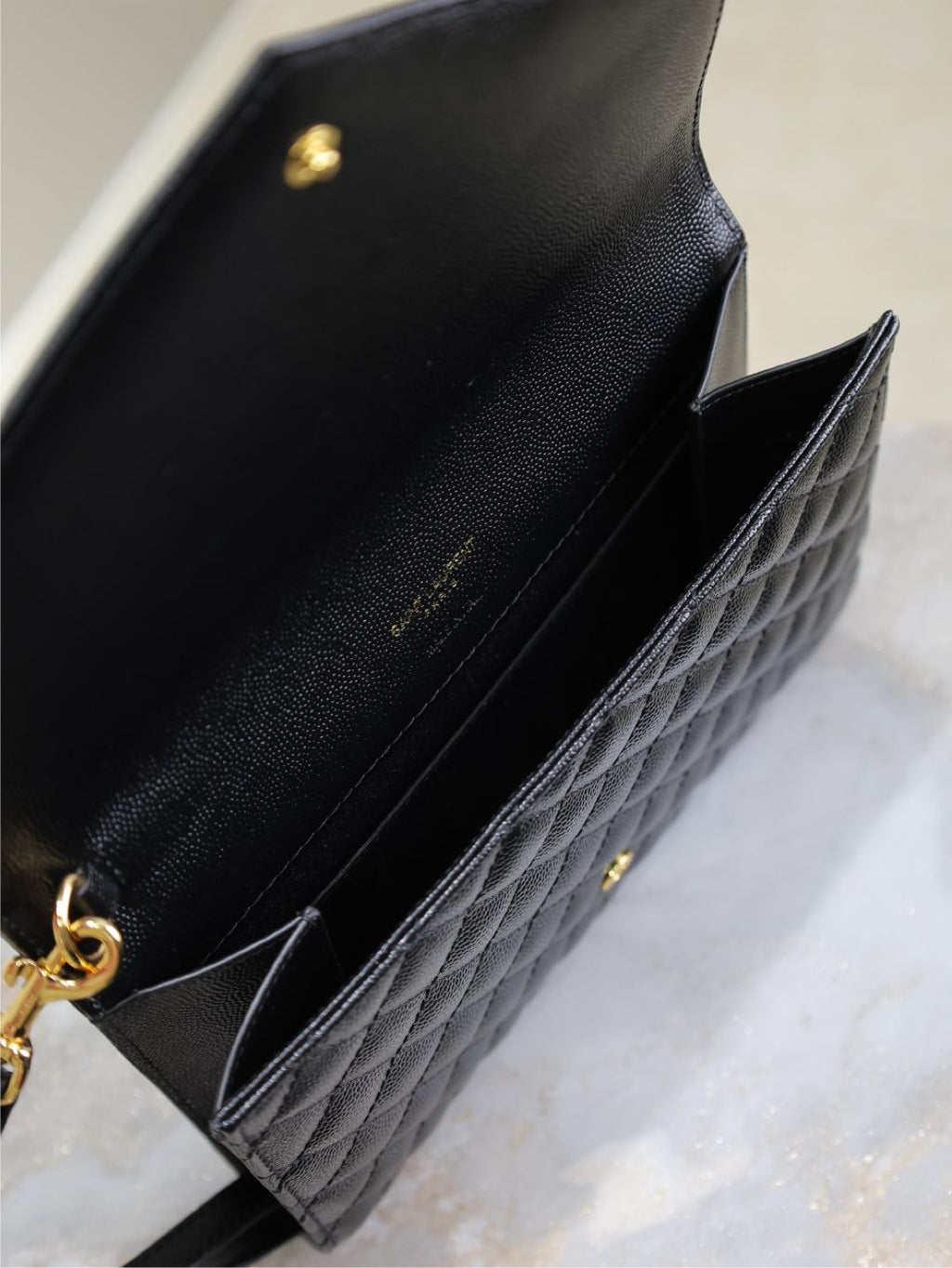 YSL small black quilted leather bag interior view with gold accents and chain strap.