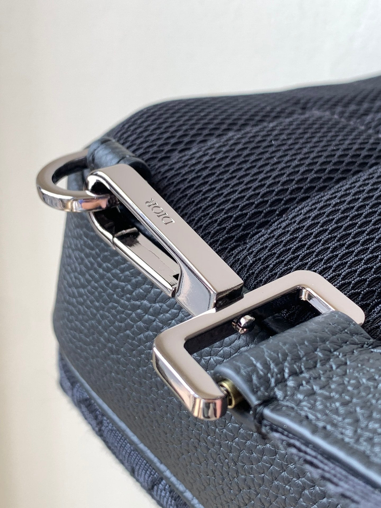 Dior mini crossbody bag close-up with silver-tone clip, zipper pull, and textured finish
