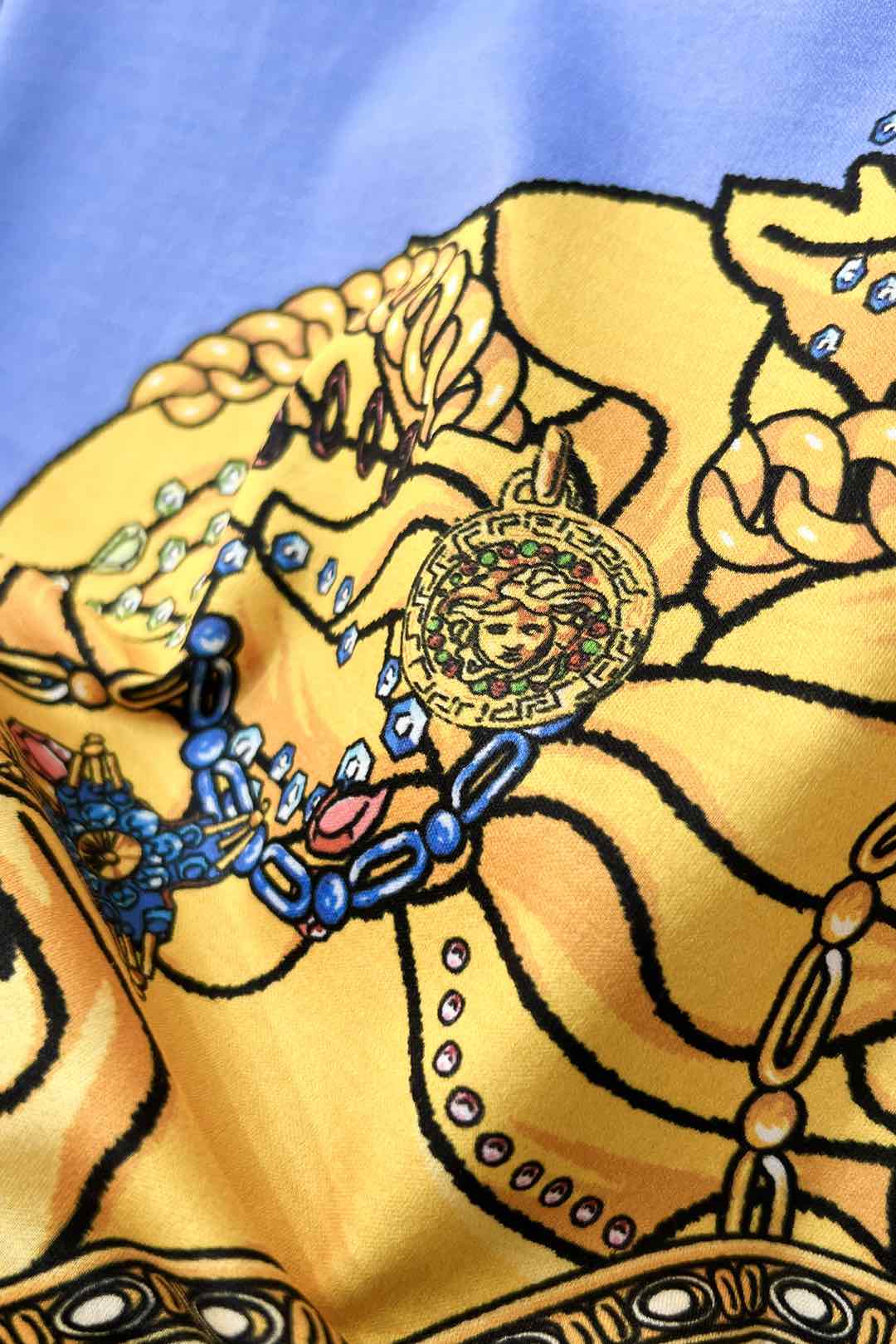 Close-up of light blue crewneck T-shirt with gold baroque figure and jeweled details