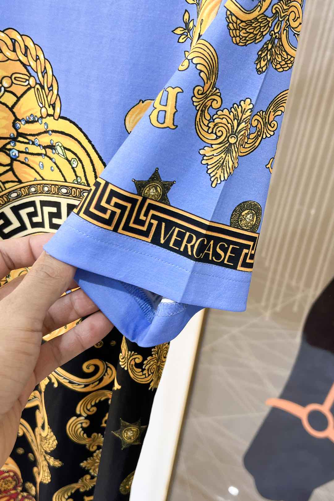 Sleeve cuff detail on light blue crewneck T-shirt with black Versace-style lettering and key
