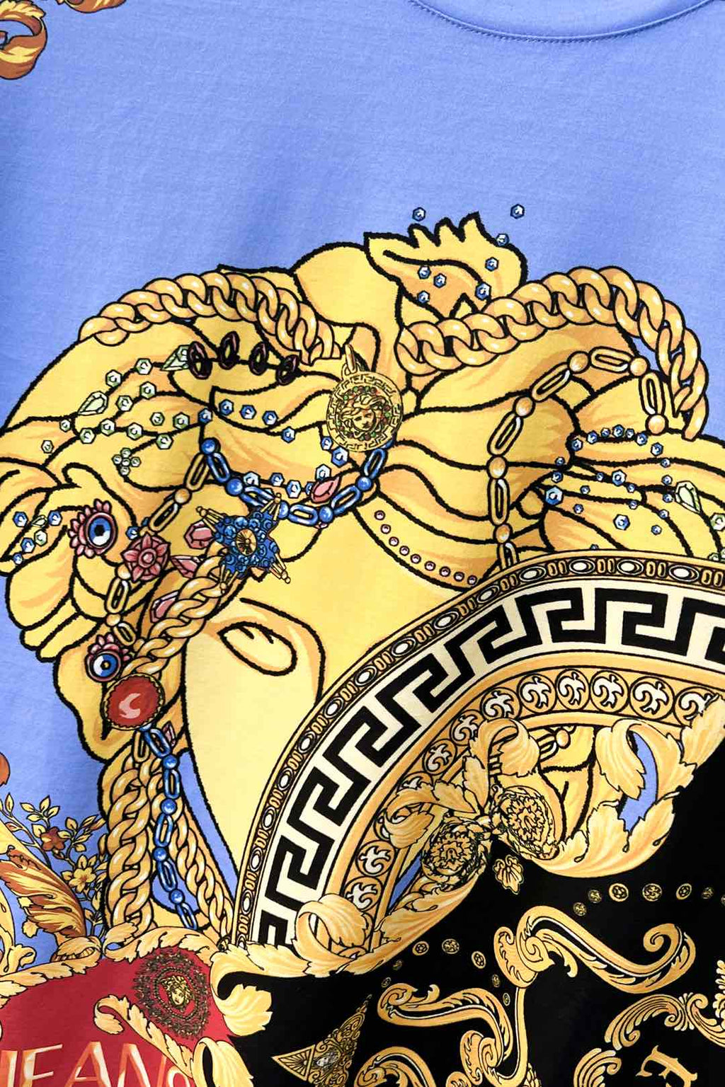 Close-up of light blue crewneck T-shirt with Medusa face graphic and Greek key trim