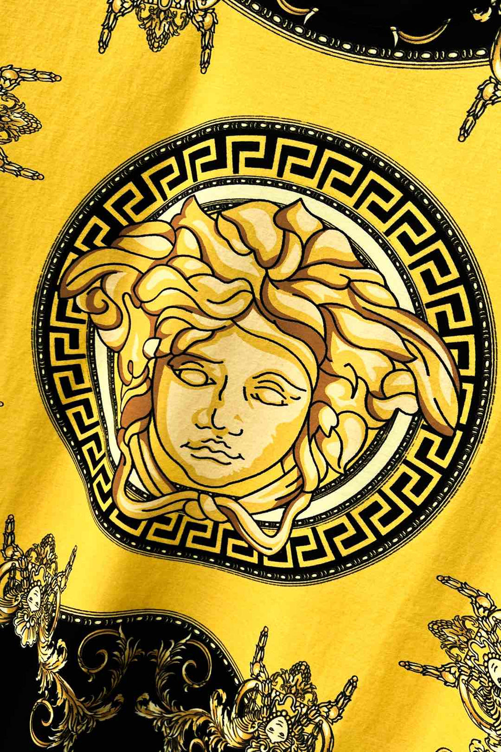 Graphic T-shirt close-up of gold Medusa-style face in black Greek key border