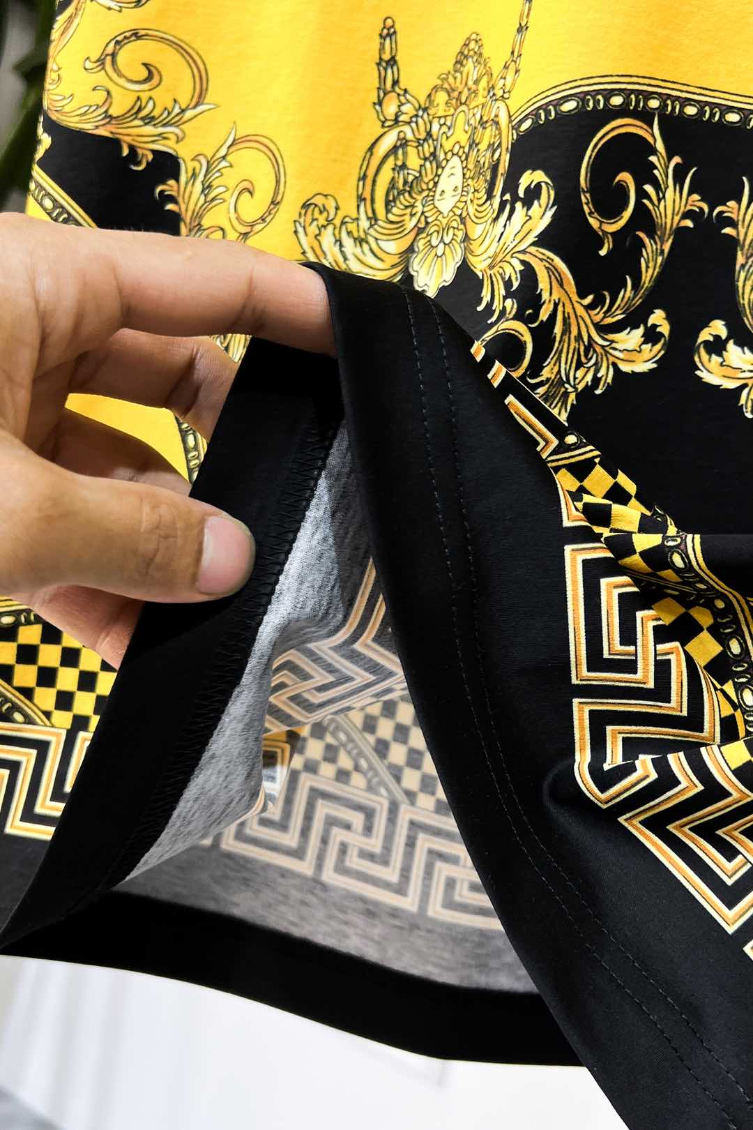 Graphic T-shirt hem and neckline seam detail in black with gold print trim
