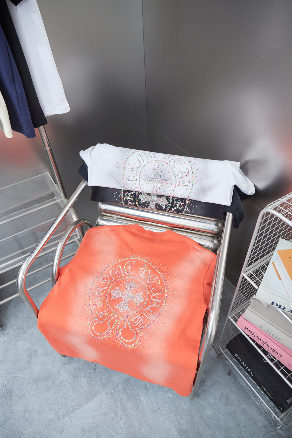Stacked folded T-shirts: coral orange with rhinestone emblem and dark graphic panel