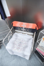 Folded white short-sleeve T-shirt with circular multicolor beaded graphic on rack