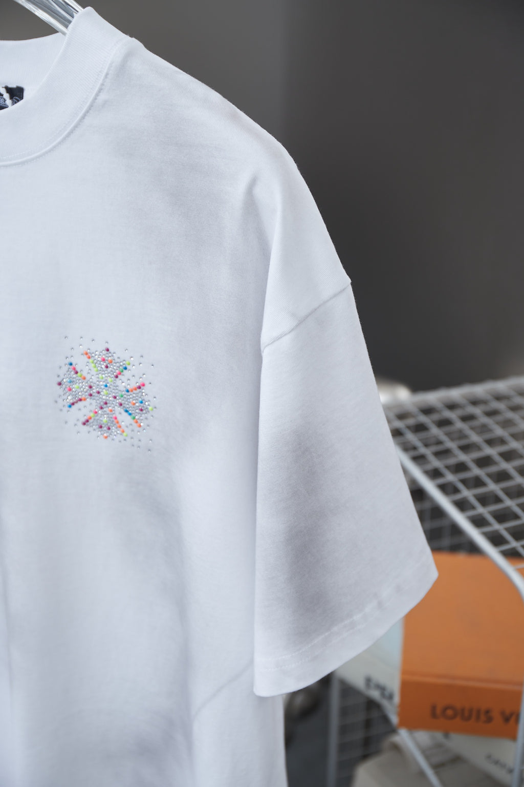 White short-sleeve T-shirt with small multicolor beaded emblem on left chest