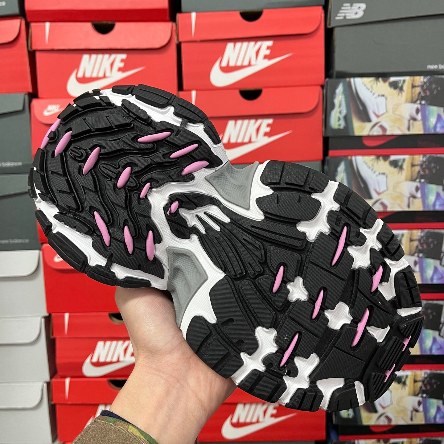 Outsole bottom of sneakers with black tread, gray platform, and pink highlights
